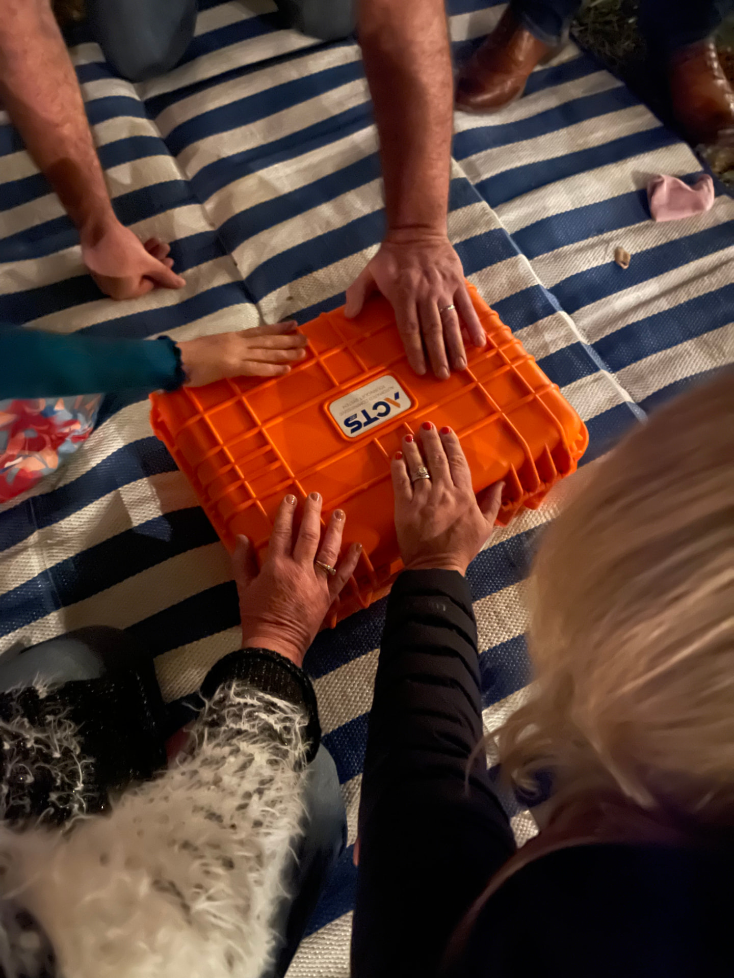 Team members gathered with hands resting on an orange ACTS tourniquet system case in prayer